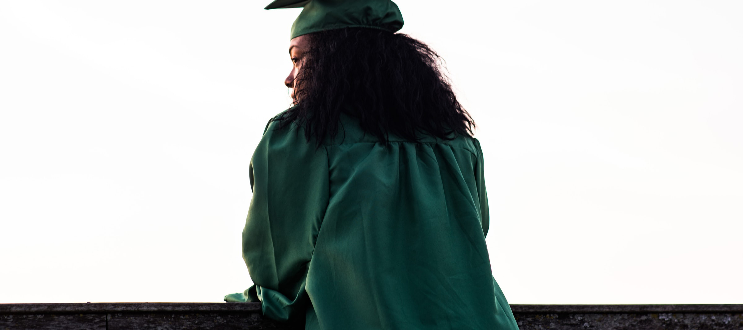 Stock photo of student in robe and graduation cap looking at a college